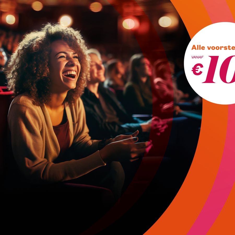 Een vrouw zit lachend op een stoel in de theaterzaal.