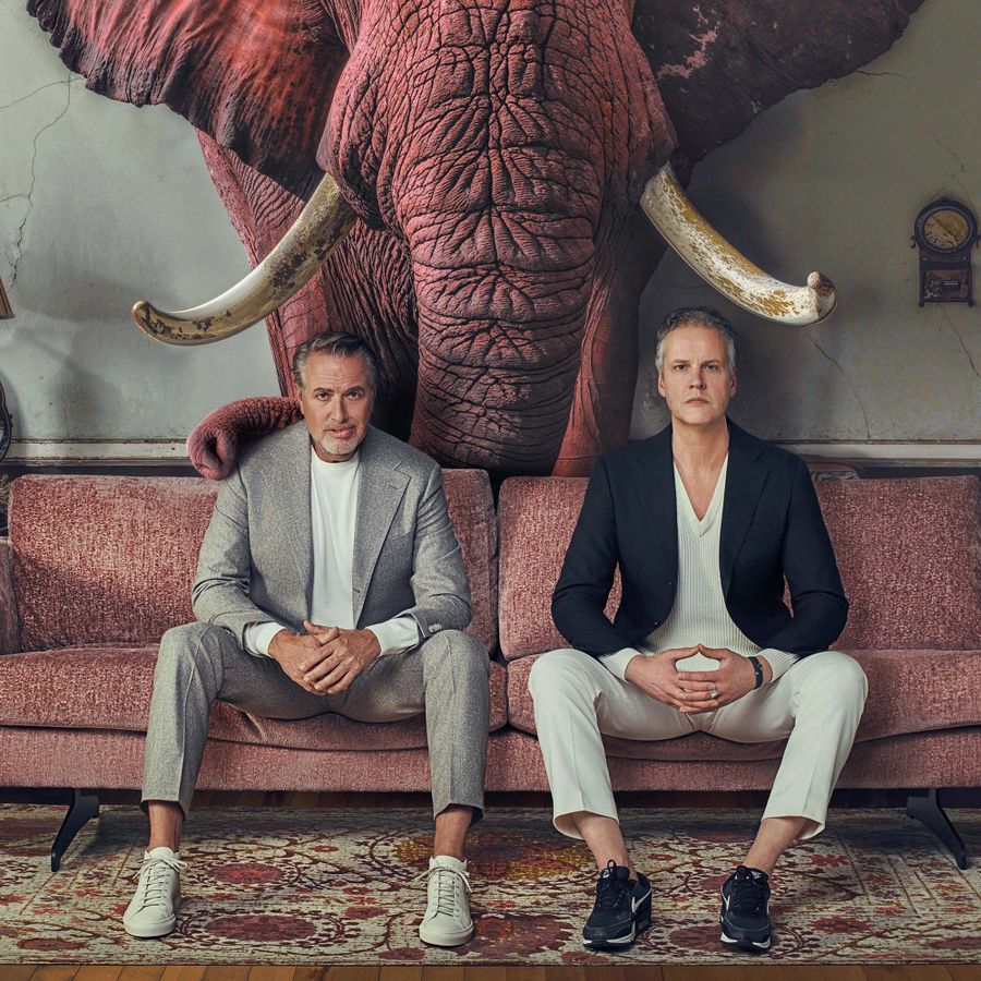 Twee mannen zitten op een bankje. Er staat een olifant achter hun.