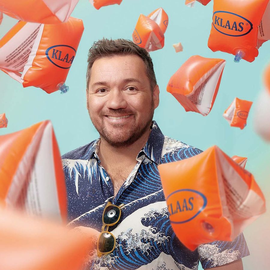 Klaas lacht naar camera, om hem heen zweven talloze oranje zwembandjes in de lucht.