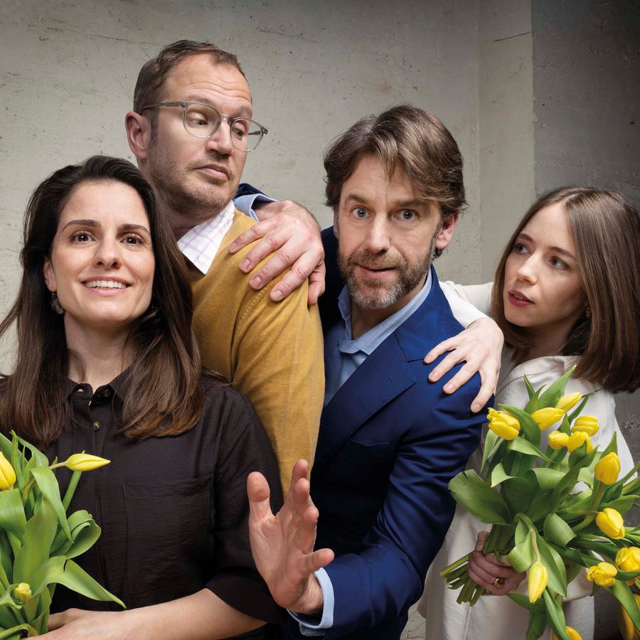 Twee mannen en twee vrouwen poseren voor een muur en hebben gele tulpen vast.