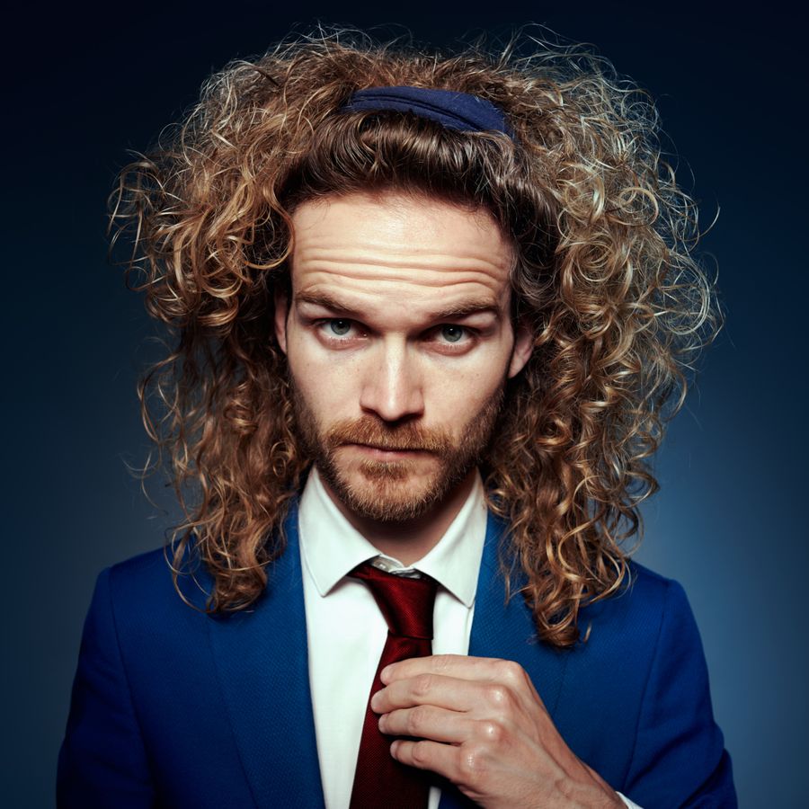 Foto van Teun met lang, krullend haar en baard en een blauwe achtergrond.