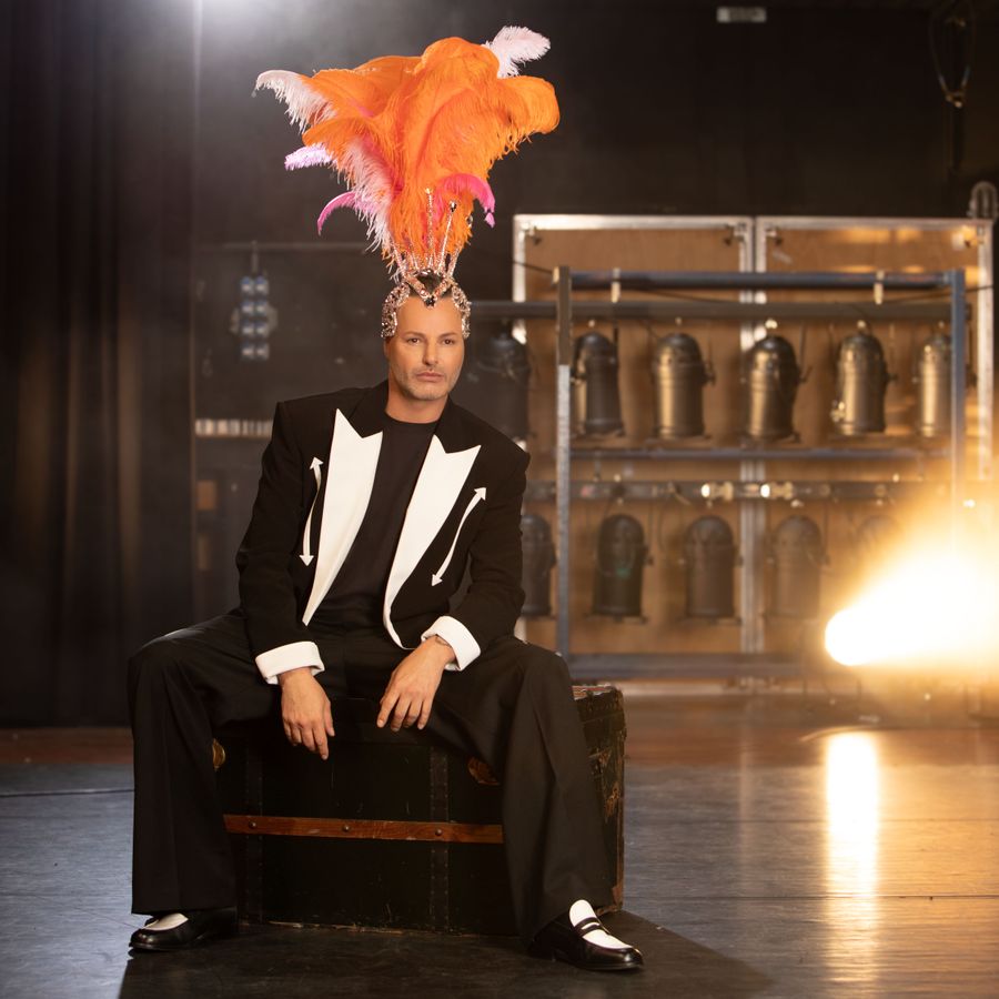 Fred zit op het podium met een hoed van veren op zijn hoofd.