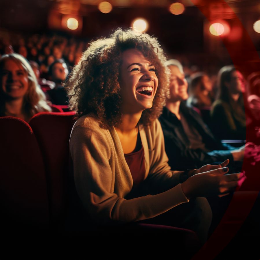 Een vrouw zit lachend op een stoel in de theaterzaal.